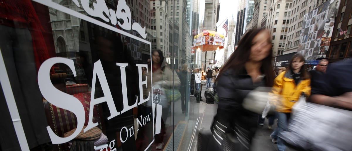 Shoppers walk down Fifth Avenue past a sale sign in the window of a Brooks Brothers store in New York