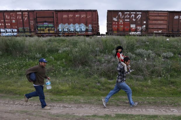 A Salvadoran father (R) carries his son while running next to another immigrant as they try to board a train heading to the Mexican-U.S. border, in Huehuetoca, near of Mexico City, June 1, 2015. An increasing number of Central Americans are sneaking across Mexico's border en route to the United States. Picture taken June 1, 2015. REUTERS/Edgard Garrido 