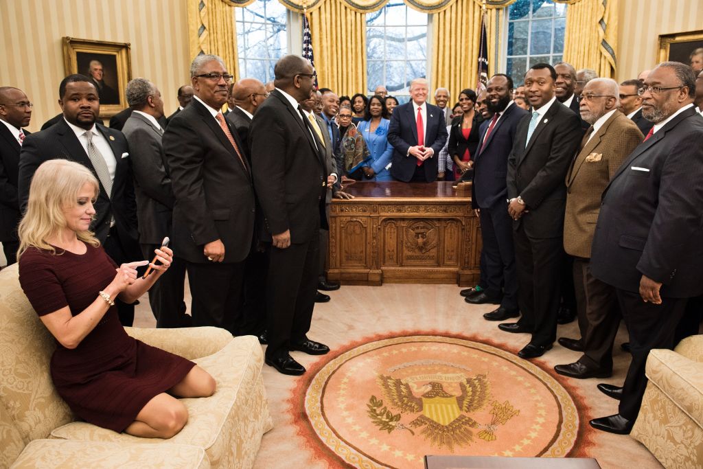 TOPSHOT - Counselor to the President Kellyanne Conway (L) checks her phone after taking a photo as US President Donald Trump and leaders of historically black universities and colleges pose for a group photo in the Oval Office of the White House before a meeting with US Vice President Mike Pence February 27, 2017 in Washington, DC. BRENDAN SMIALOWSKI/AFP/Getty Images