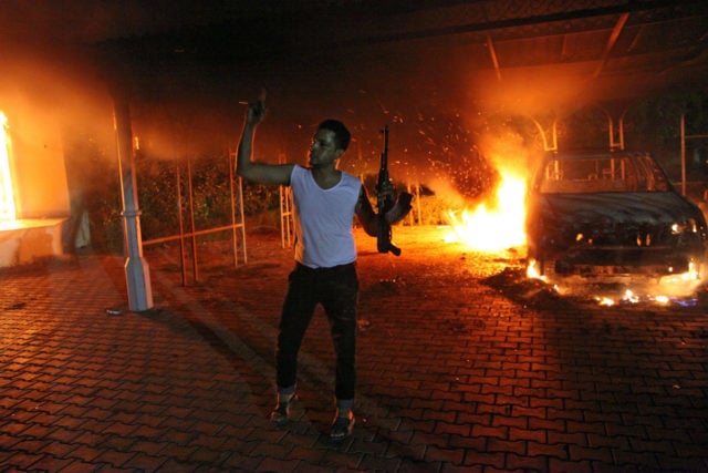An armed man waves his rifle as buildings and cars are engulfed in flames after being set on fire inside the US consulate compound in Benghazi late on September 11, 2012. An armed mob protesting over a film they said offended Islam, attacked the US consulate in Benghazi and set fire to the building, killing one American, witnesses and officials said. (Photo credit should read STR/AFP/GettyImages)