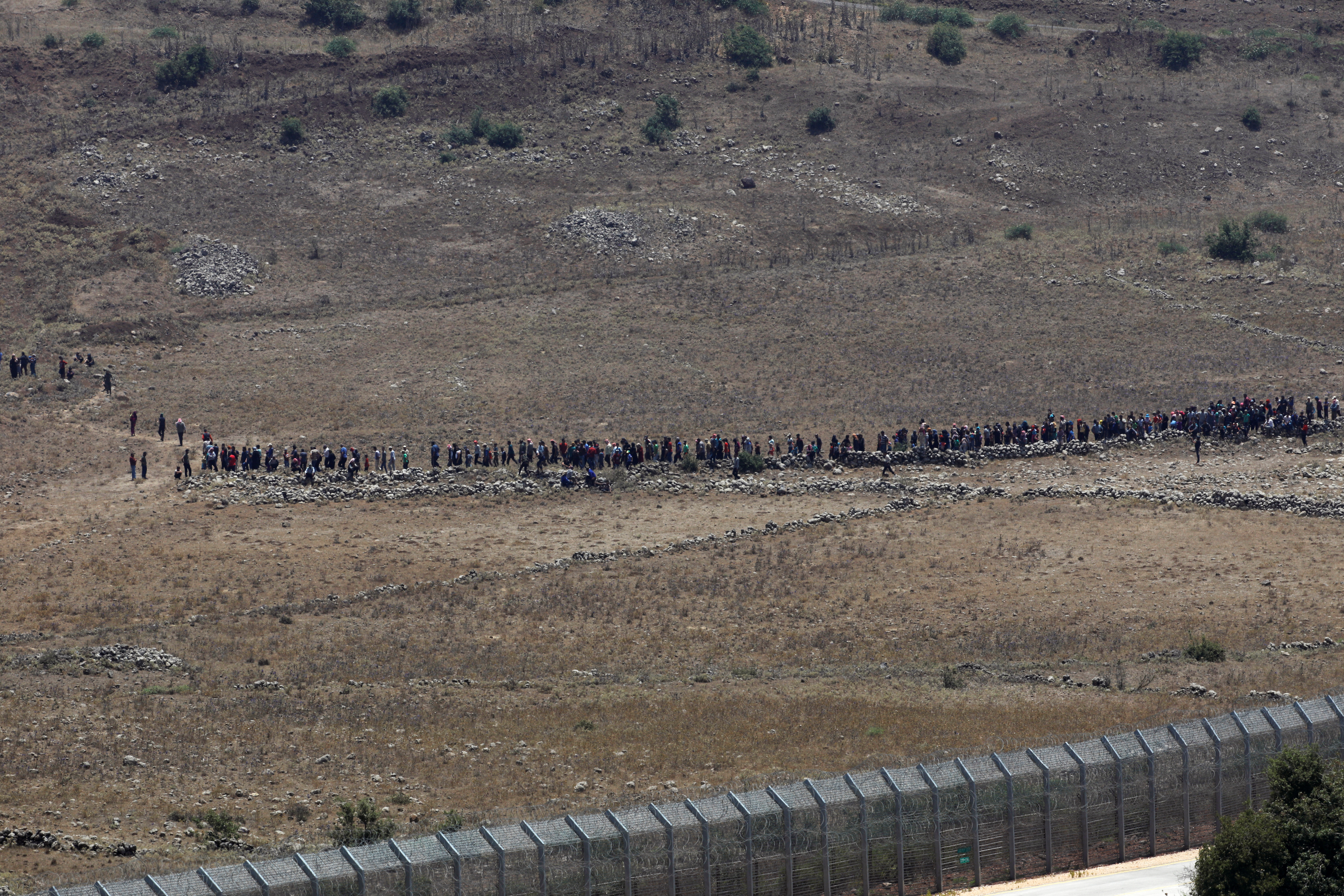 People start to walk away from the border fence between Israel and Syria at its Syrian side as it is seen from the Israeli-occupied Golan Heights near the Israeli Syrian border July 17, 2018. REUTERS/Ronen Zvulun - RC12E6DB43B0